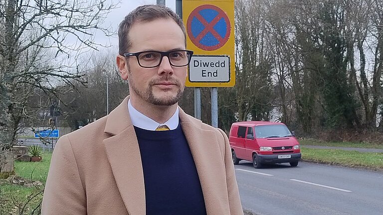Candidate James Rigby standing with a speeding sign